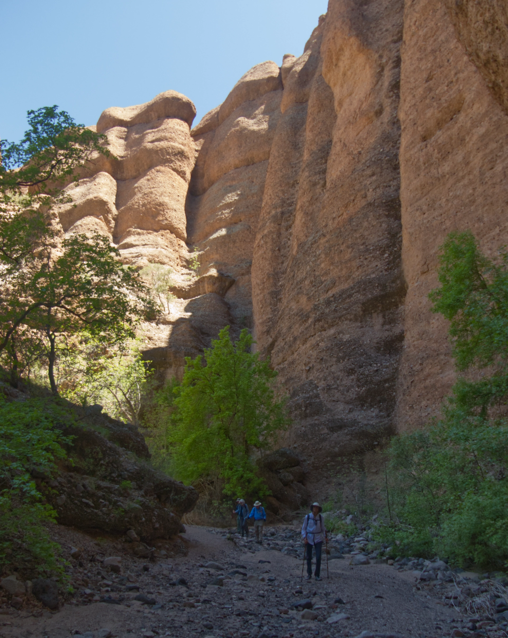three hikers in deep shade below towering cliffs