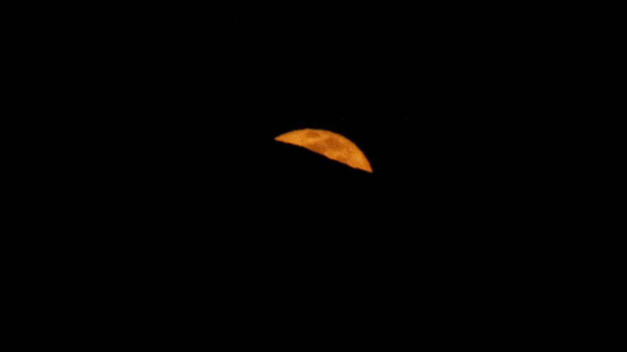 a sliver of orange moon behind the mountains